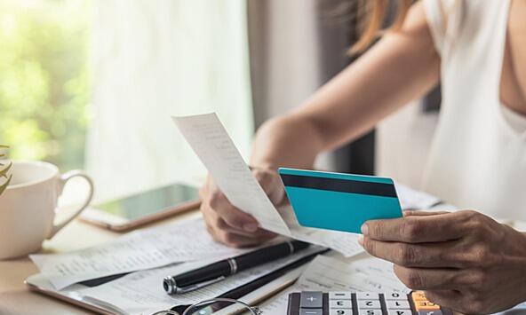 Woman checking her credit card receipts at a desk with calculator, coffee cup and reading glasses.